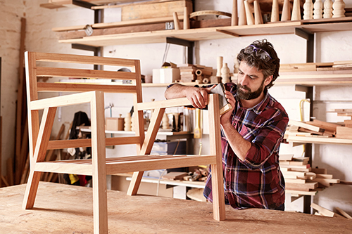 Photograph of a man sanding a wood chair frame